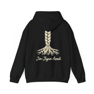 May include: Black hoodie with a cream-coloured braid design that transforms into roots. The text "Jin Jiyan Azadi" is printed in cream-coloured script below the roots. The hoodie has a hood and long sleeves.