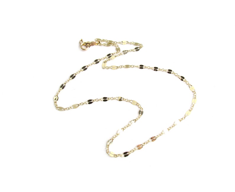 May include: A delicate gold necklace with a repeating oval link design. The necklace is displayed on a white background, showcasing its intricate pattern and the warm tone of the metal. The clasp is visible at the top.