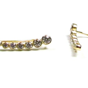 May include: A pair of gold ear cuffs with a row of clear round stones. The ear cuffs are curved and have a hook closure.