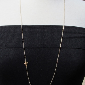 May include: A gold chain necklace with a small cross pendant. The necklace is on a white mannequin with a black top.