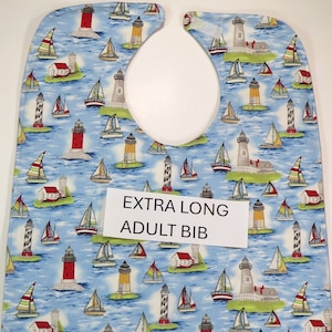 May include: A blue and white adult bib with a lighthouse and sailboat pattern. The bib is extra long and has a neck opening. The text "EXTRA LONG ADULT BIB" is printed on a white label.