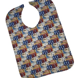 May include: A red, white, and blue patterned bib with a large opening for the neck. The pattern features American flags, stars, and the words "Liberty and Justice for All".