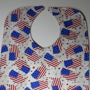 May include: A white bib with a red, white, and blue American flag pattern. The bib has a rounded neck opening and is made of fabric.