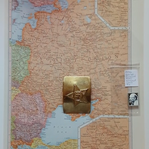 May include: A vintage map of the Western Soviet Union from 1970, showing the borders of the Soviet republics. A gold metal star with a hammer and sickle design is placed on the map. The text "1970 Soviet Communist Party Emblem" is written on a white piece of paper.