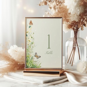 May include: A gold-framed table number card with a green background and white flowers, butterflies, and the number "1" with the word "Table" underneath.