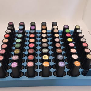 May include: A blue organizer tray filled with black nail polish bottles. The bottles have colorful tops and are arranged in a honeycomb pattern. Each bottle is labeled with a number and a color.