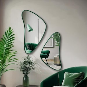 May include: A green velvet armchair with a pillow sits in front of a wall with two green abstract mirrors. The room has a green rug and a potted plant.