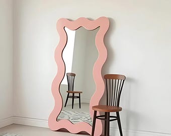 May include: A pink wavy framed full-length mirror with a black and brown wooden chair in front of it.