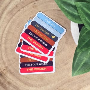 May include: A stack of book-themed stickers with titles like "Firefly Lane", "Winter Garden", "The Nightingale", "The Great Alone", "The Four Winds", and "The Women".