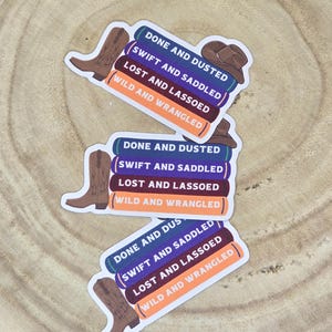 May include: Three colorful stickers with a cowboy boot design. Each sticker has the text "Done and Dusted", "Swift and Saddled", "Lost and Lassoed", and "Wild and Wrangled" stacked on top of each other.