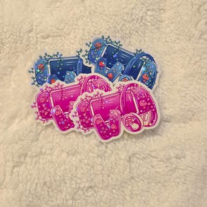 May include: Two vinyl stickers featuring a pink and blue Nintendo Switch console with a floral design. The stickers have a glittery finish.