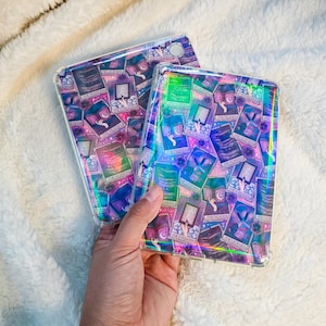 May include: Two clear tablet cases with a colorful tarot card design. The cases feature a holographic effect, with a pattern of tarot cards in shades of purple, blue, and green. The cases are held by a hand.