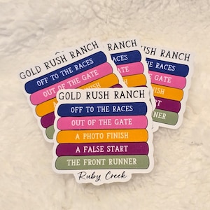 May include: Five colorful stickers with the text "Gold Rush Ranch" and phrases related to horse racing, such as "Off to the Races", "Out of the Gate", and "A Photo Finish". The stickers are stacked on top of each other and have a white background.