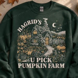 May include: A dark green crewneck sweatshirt featuring a graphic illustration of a stone cottage surrounded by pumpkins and a wheelbarrow. The text reads HAGRID'S U PICK PUMPKIN FARM in a cream-colored font, with a crescent moon and stars above.