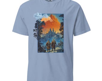 May include: A light blue t-shirt featuring a graphic print of two figures walking towards a castle in a fantasy landscape. The castle is situated on a mountain with a red and orange sky behind it.