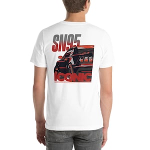 May include: White t-shirt with a graphic of a black car and red detailing. The text "SN95" is above the car, and "ICONIC" is below it. The shirt is made of a soft material.