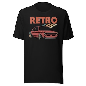 以下が含まれることがあります： 赤、オレンジ、青色のレトロカーグラフィックが特徴の黒いTシャツ。「RETRO」の文字が車の真上にプリントされています。このデザインは、ヴィンテージクラシックカーをテーマにしています。