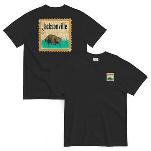 May include: Black t-shirts with a Jacksonville stamp design. The stamp features a brown animal in green grass with the word "Jacksonville" above. One shirt has the stamp on the back, the other on the front.