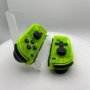 May include: Two bright green translucent Nintendo Switch Joy-Con controllers with black buttons and analog sticks.