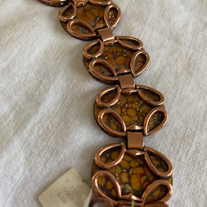 May include: A vintage copper-coloured bracelet with oval links. Each link features a mottled, yellow, brown, and red design. The bracelet is connected by copper-coloured loops and rectangular clasps. A price tag is attached.