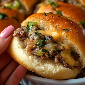 Peut inclure: Gros plan sur un slider garni de bœuf et de fromage, recouvert de persil. Le slider est tenu dans une main.