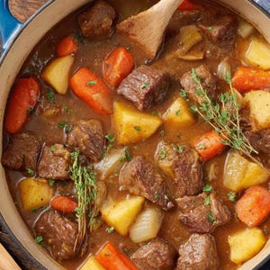 May include: A hearty beef stew in a blue enameled cast iron pot. The stew features large chunks of beef, carrots, potatoes, and onions in a rich brown gravy. Fresh thyme sprigs and parsley garnish the dish, with a wooden spoon resting inside.