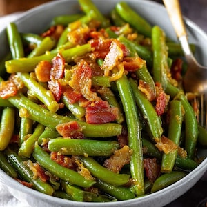 May include: A bowl of green beans topped with crispy bacon. The green beans are bright green and appear to be cooked. The bacon is a mix of red and brown, with a slightly crispy texture. A gold-colored fork is visible.