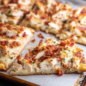May include: A close-up shot of a sliced pizza with chicken and bacon toppings. The pizza has a golden-brown crust and is topped with melted cheese, pieces of cooked chicken, and crispy bacon. Sprigs of green herbs are sprinkled on top.