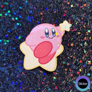 May include: A pink and white cartoon character sticker with a star shape. The character has a pink body with a red heart-shaped belly and a yellow star on its head. The character is smiling and has big eyes.