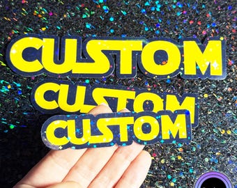 May include: Yellow "CUSTOM" stickers with a blue outline and glitter accents. The stickers are on a sparkly, dark background. The word "Sticker" is in a circular logo in the bottom right corner.