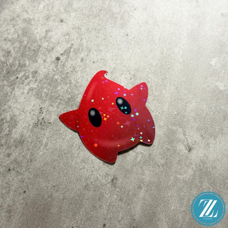May include: A red star-shaped sticker with black oval eyes and a glittery, holographic finish. The sticker has a cartoonish design with a gradient effect, and is likely a decorative item or a collectible.