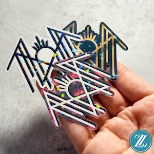 May include: Three geometric stickers with a sunburst design. The stickers feature a white and black striped pattern with a holographic effect. One sticker has a dark teal background with gold accents, another has a pink and black floral background.