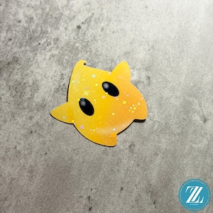 May include: A yellow star-shaped sticker with black oval eyes and a small loop at the top. The sticker has a gradient effect, transitioning from yellow to orange, and is decorated with small star-shaped sparkles.