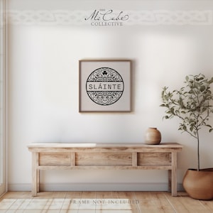 May include: A square wall art print featuring a black circular design with intricate Celtic knotwork patterns and a small shamrock icon at the top. The word SL&Aacute;INTE is printed in bold black capital letters across the center of the circle.