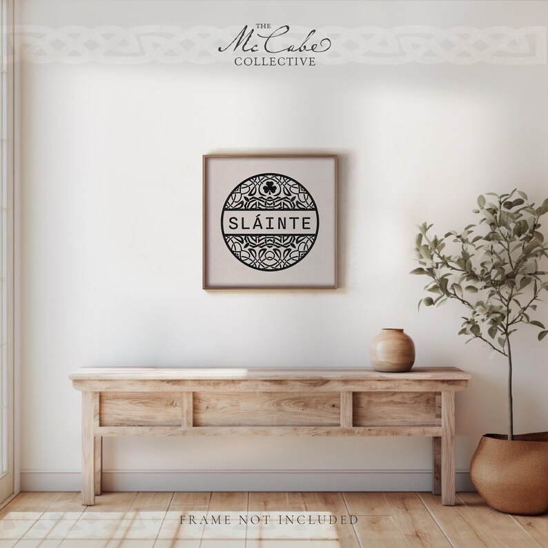 May include: A square wall art print featuring a black circular design with intricate Celtic knotwork patterns and a small shamrock icon at the top. The word SL&Aacute;INTE is printed in bold black capital letters across the center of the circle.