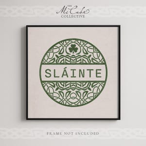 May include: A square wall art print featuring a dark green circular emblem with intricate Celtic knotwork patterns and a shamrock icon. The word SL&Aacute;INTE is printed in a horizontal band across the center. The text THE MCCABE COLLECTIVE appears above and FRAME NOT INCLUDED below.