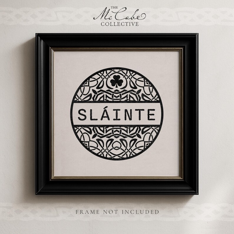 May include: A square black frame containing a white print with a circular black design featuring intricate knotwork, a shamrock icon, and the text SL&Aacute;INTE in the center. The text THE MCCABE COLLECTIVE appears above the frame and FRAME NOT INCLUDED below.