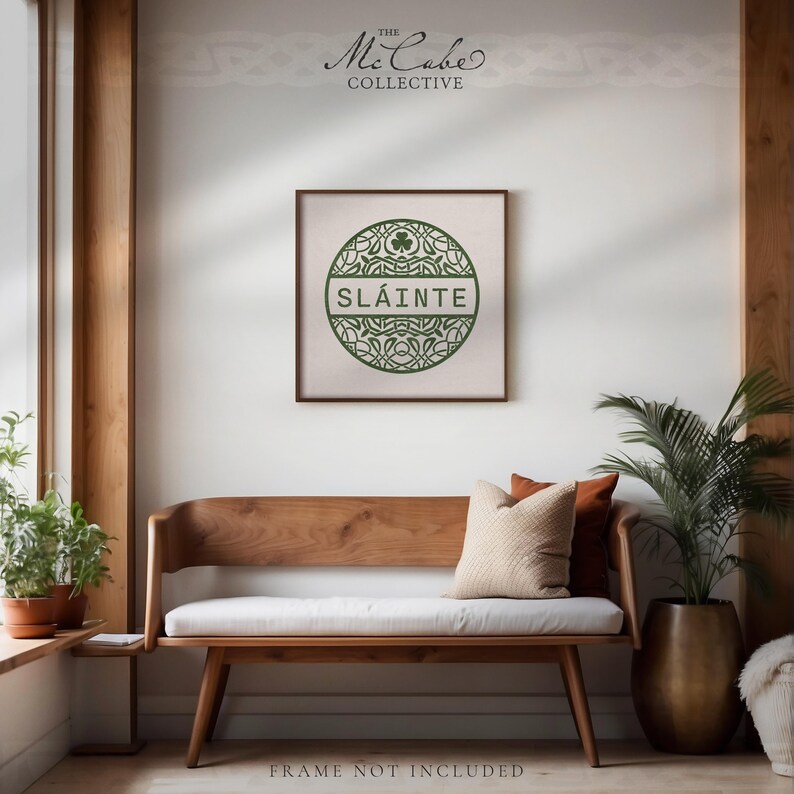 May include: A square wall art print featuring a circular green Celtic knot design with a shamrock at the top and the text SL&Aacute;INTE in the center. The print is displayed above a wooden bench with a white cushion and two throw pillows.
