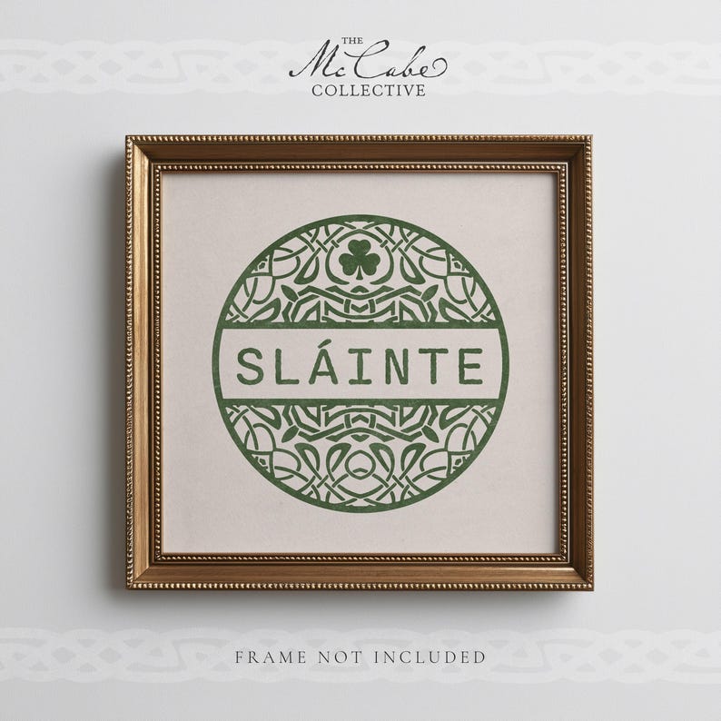 May include: A square wall art print in a gold frame featuring a green circular design with intricate knotwork, a shamrock icon, and the text SL&Aacute;INTE in the center. Above the frame is the text THE MCCABE COLLECTIVE and below is FRAME NOT INCLUDED.