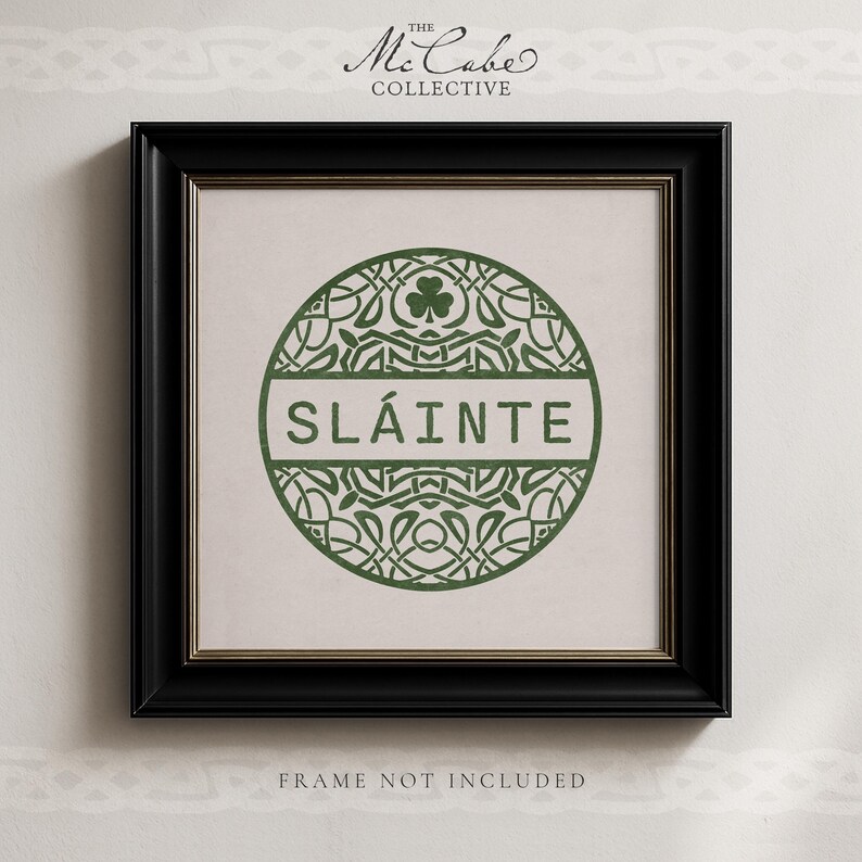 May include: A square black frame containing a print with a circular green Celtic knot design. The center features the word SL&Aacute;INTE in green capital letters. Above the text is a small shamrock. The text THE MCCABE COLLECTIVE is at the top.