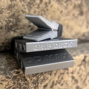 Puede incluir: Tres objetos rectangulares de color plateado apilados uno encima del otro. El objeto superior tiene una pieza articulada y en &aacute;ngulo. El objeto del medio est&aacute; etiquetado "GRIP DECK" y el inferior "GD MAX".