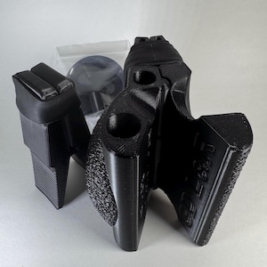 Puede incluir: Accesorios de pistola negros impresos en 3D, que incluyen una empuñadura y otros componentes. Los artículos tienen una superficie texturizada y parecen estar hechos de plástico. La imagen está tomada sobre un fondo blanco liso.