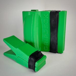 May include: Green Gripdeck tool with a black band, next to a larger green Gripdeck tool. The smaller tool is open, resembling a clothespin. The text "GRIPDECK" is visible on the side of the larger tool.
