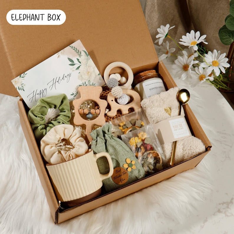 May include: A gift box labeled "Elephant Box" filled with various items. Includes a greeting card, wooden toys, scrunchies, a mug, a candle, a spoon, and a pair of socks. The card reads "Happy Holidays".
