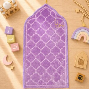 May include: A rectangular prayer mat in a vibrant purple hue featuring a repeating quatrefoil pattern, a pointed arch top with a small yellow tassel, and a yellow fringed bottom edge. The mat is surrounded by wooden blocks and beads.