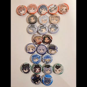 Puede incluir: Una colección de botones redondos y coloridos con ilustraciones de personajes de estilo anime. Los botones varían en diseño, con diferentes personajes y combinaciones de colores. Los botones están dispuestos sobre una superficie blanca.