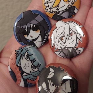 May include: Five round button pins featuring anime-style characters. The characters are drawn in black and white with colorful backgrounds. The characters have different hairstyles and expressions.