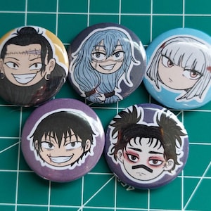 May include: Five circular badges featuring anime-style character illustrations. The badges showcase different characters with unique facial expressions and hairstyles, set against yellow, blue, and purple backgrounds. They are arranged on a green grid.
