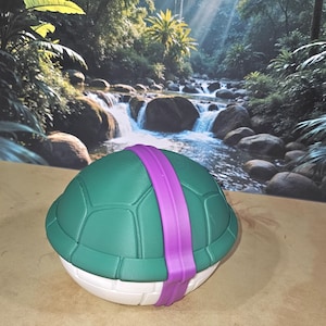 May include: A green and white turtle shell with a purple band. The shell has a textured surface and is designed to resemble a turtle's back. The background features a tropical scene with a waterfall and lush greenery.