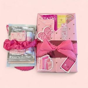 May include: A pink gift box wrapped with pink paper and a pink ribbon. The box is decorated with stickers that say "Hot girls Read books", and "Bookstore". The box contains beauty products and books.
